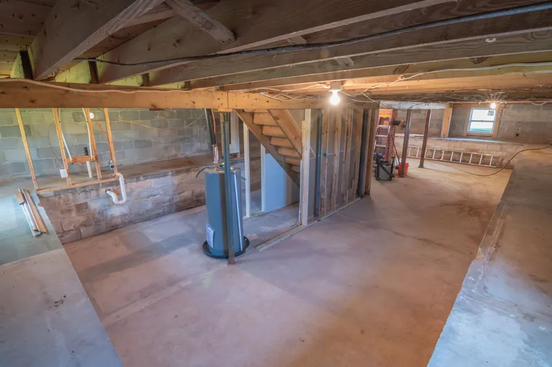 Unfinished basement with wooden beams, exposed pipes and a water heater
